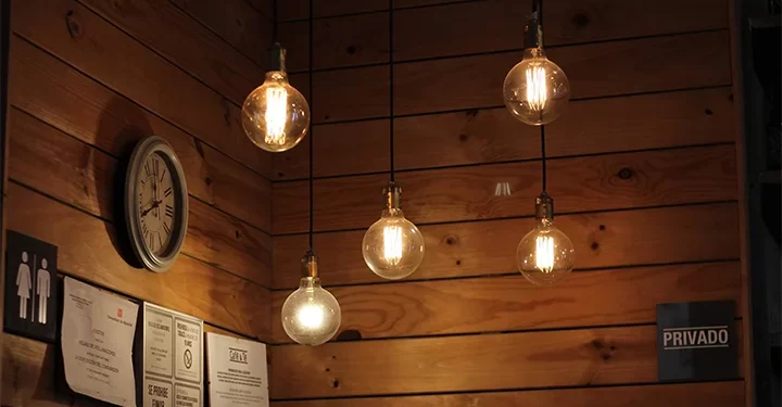 لامپ های رشته ای به کار رفته در یک کافه با دیوار های چوبی و ساعتی نصب شده بر روی دیوار. در مقایسه انواع لامپ، رشته ای ها بیشتر نقش مکمل را دارند نه نور اصلی.