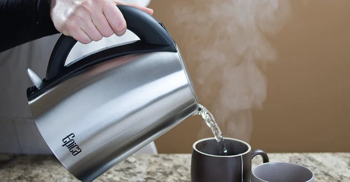 فردی در حال ریختن آب جوش درون یک لیوان به واسطه یک چای ساز استند دار با بدنه آلومینیومی می‌باشد.