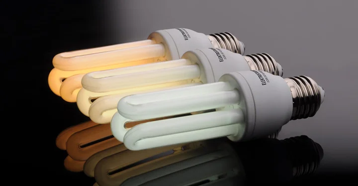 لامپ های کم مصرف به رنگ های خنثی، مهتابی و آفتابی که بر روی یک سطح شیشه ای قرار گرفته اند.
