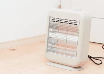 بخاری برقی تابشی سفید که بر روی یک پارکت به رنگ کرمی قرار گرفته است و سیم مشکی آن در پشت آن قرار دارد.