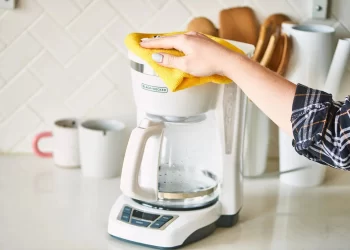 فردی در حال تمیز کردن یک دستگاه قهوه ساز سفید رنگ است. | مجله برقیجات