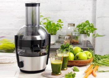 یک آبمیوه گیری که بر روی یک میز در کنار سیب های سبز قرار دارد.